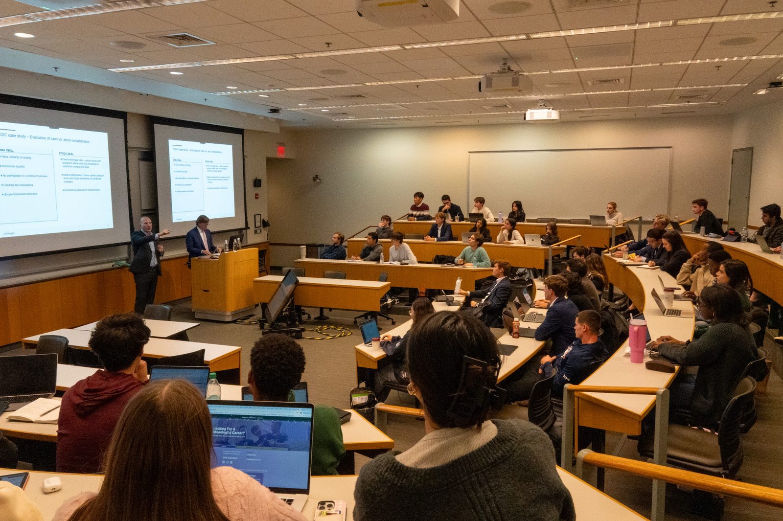 A speaker presenting to a full lecture hall of students.
