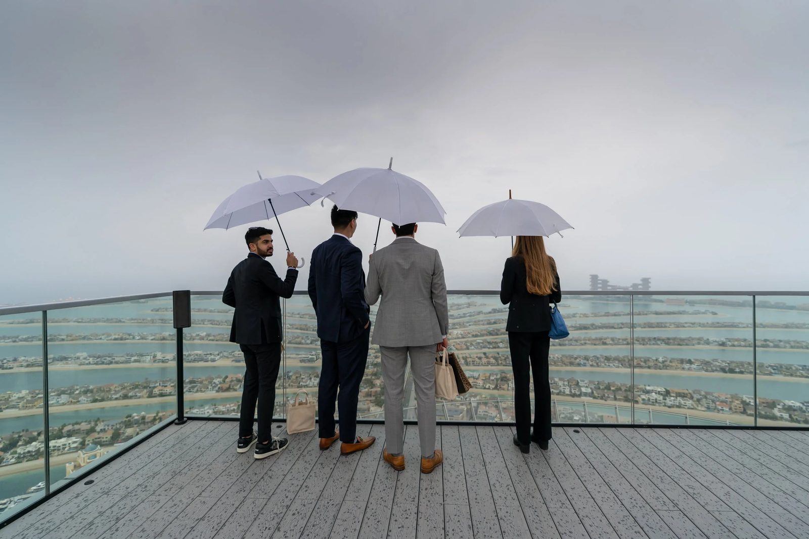 Four members under white umbrellas looking out over Palm Jumeirah from a rooftop in Dubai.